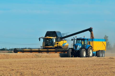 Combine harvester harvesting wheat whilst offloading grain into a grain trailer driving alongside.